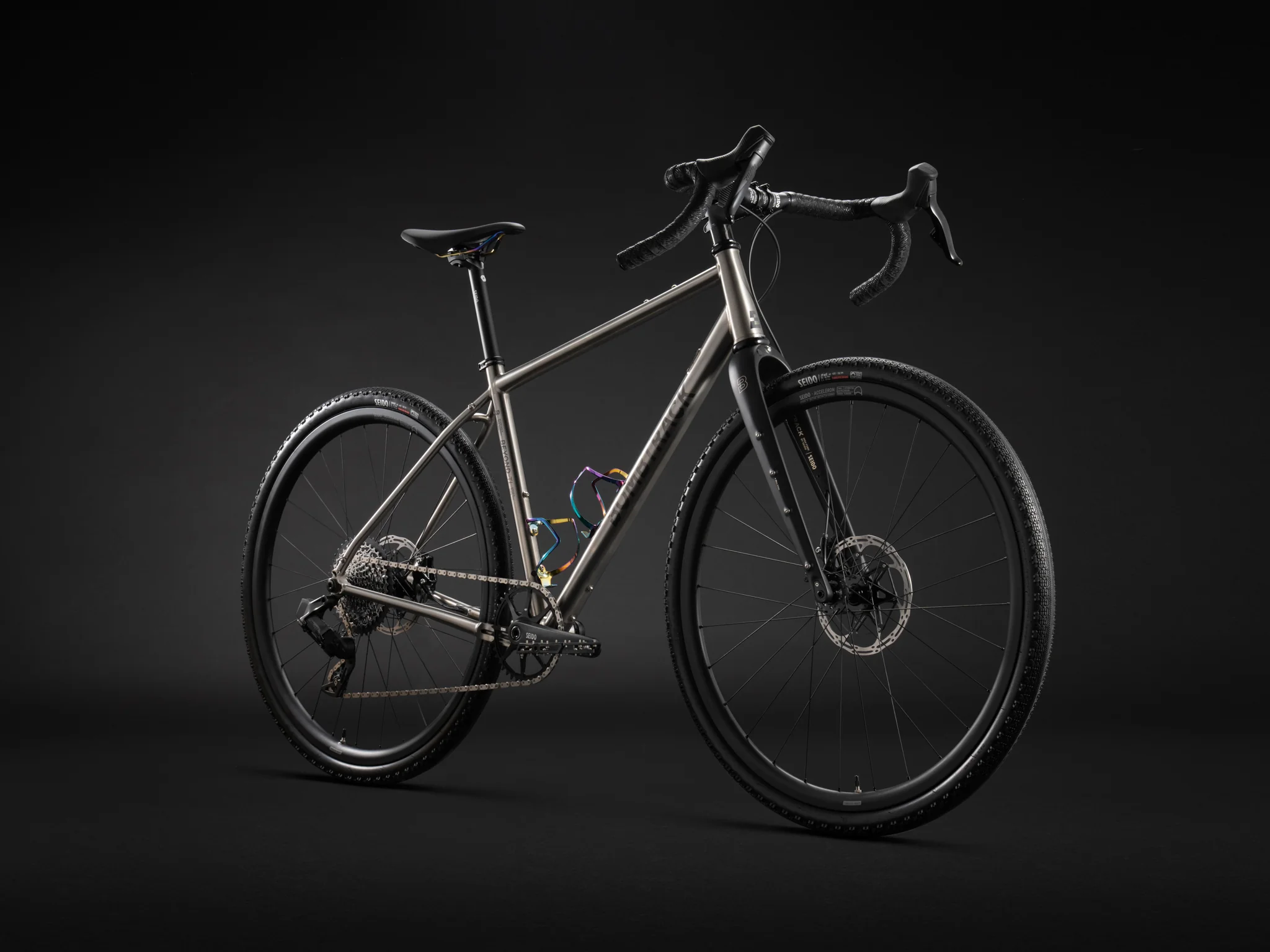 Sleek profile of a titanium Bombtrack gravel bike against a solid black background.
