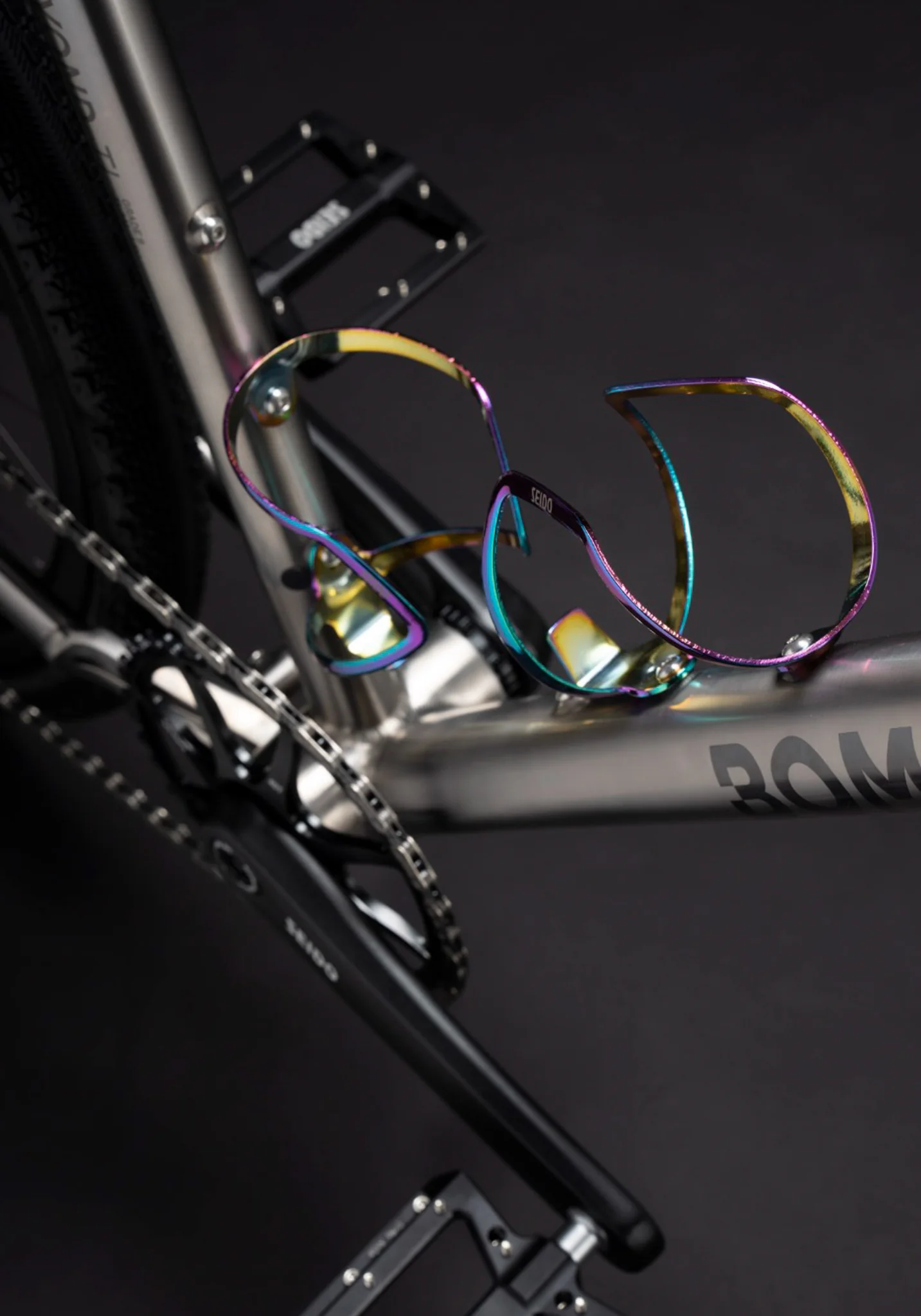 Macro shot of a rainbow-colored iridescent bottle cage on a titanium bike frame.