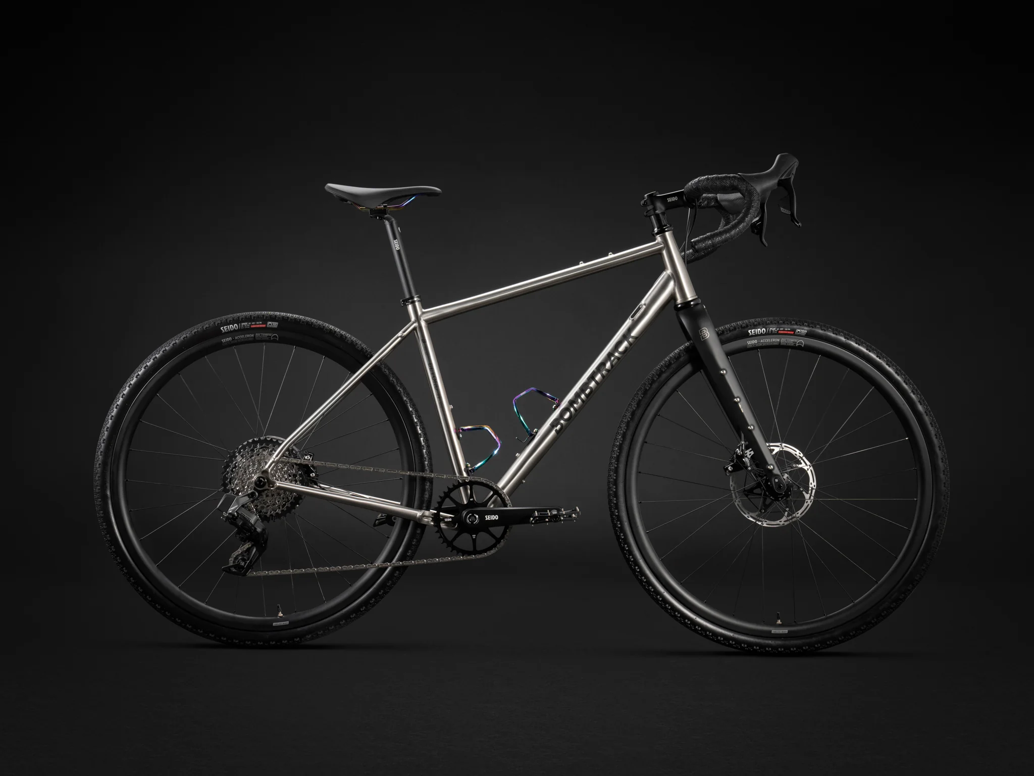 Profile view of a titanium Bombtrack gravel bike with carbon forks on a dark background.
