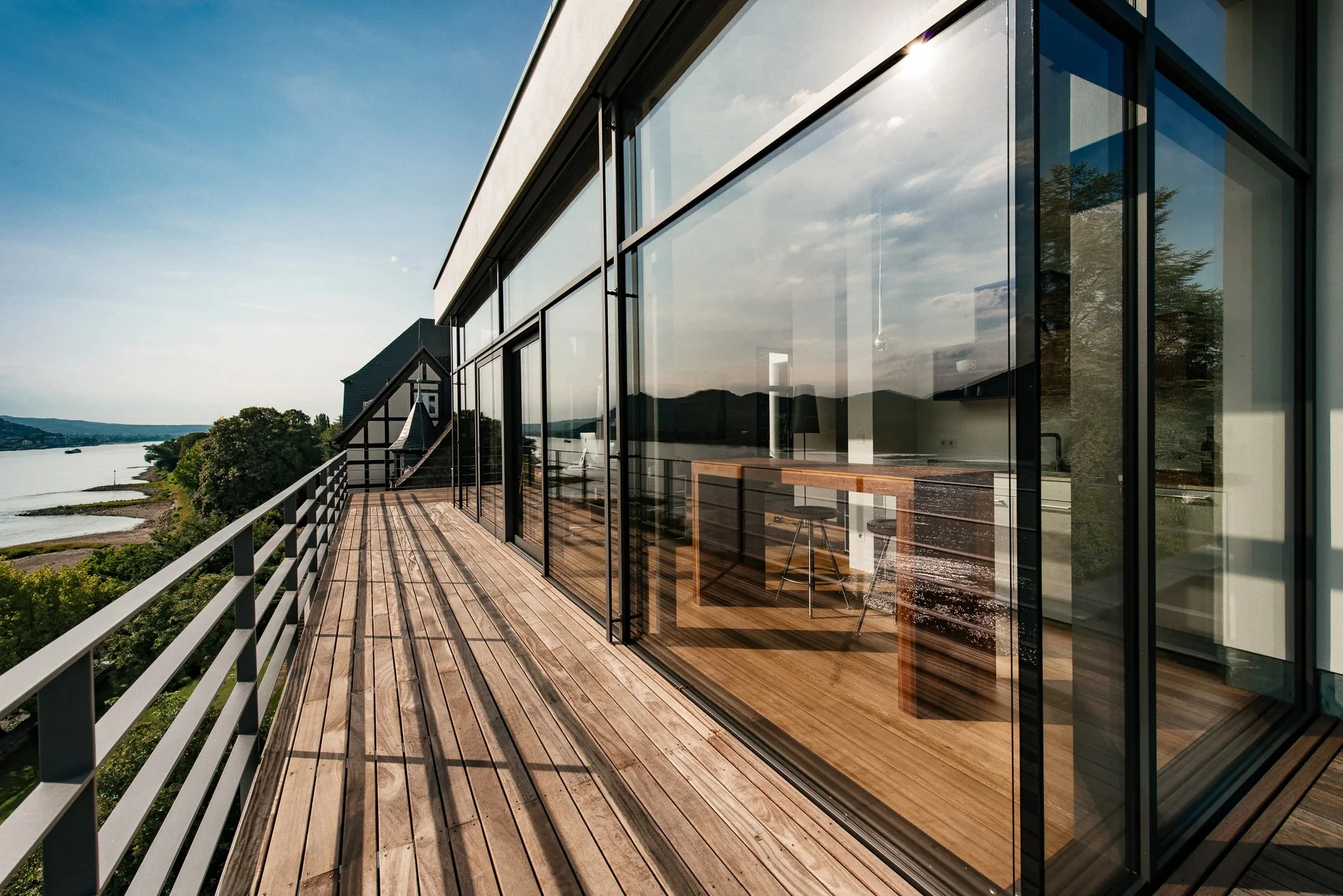 Long wooden balcony with metal railings alongside the villa's glass facade.